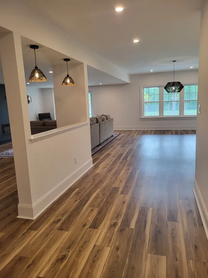 Finished basement with wood-look flooring, pendant lighting, and large windows
